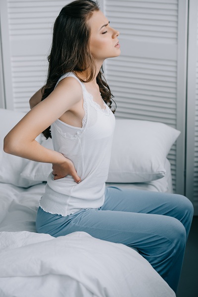 Young woman in pyjamas suffering from lower back pain